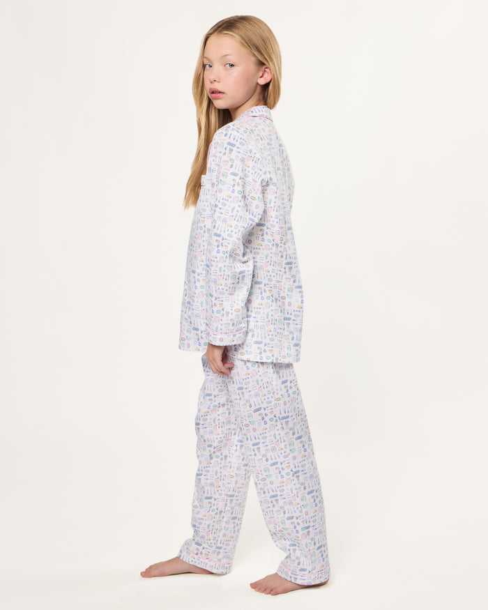 The Kid's Twill Pajama Set in Baking Spirits Bright features white long-sleeve button-up top and long pants with a colorful print of various small household and travel items.