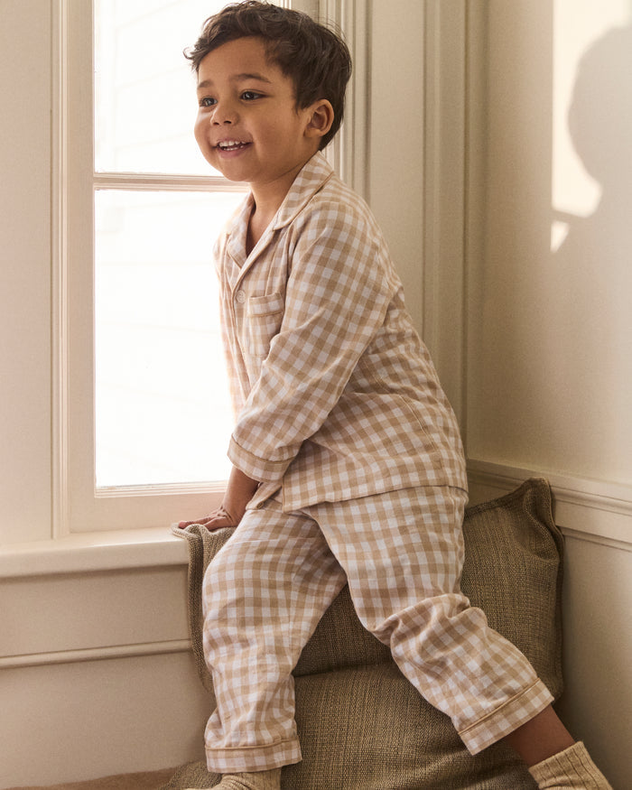 Kid's Twill Pajama Set in Camel Gingham features long sleeves, pants with an elastic waistband, and a button-up shirt with a collar and front pocket, all in a beige and white gingham check pattern.