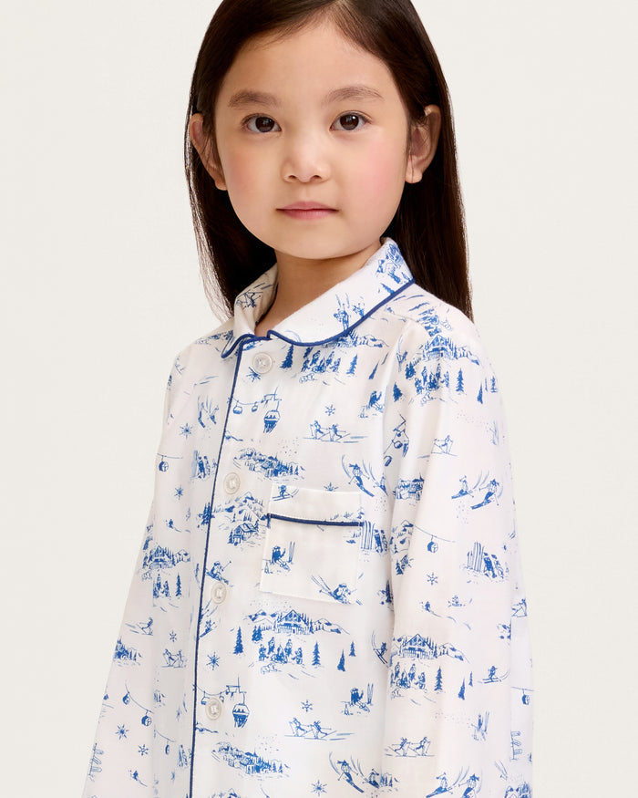 Kid's Twill Pajama Set in Chalet Toile, a white pajama set with blue piping and scenic print, includes a long-sleeve button-up top and matching pants, shown laid flat on a white background.