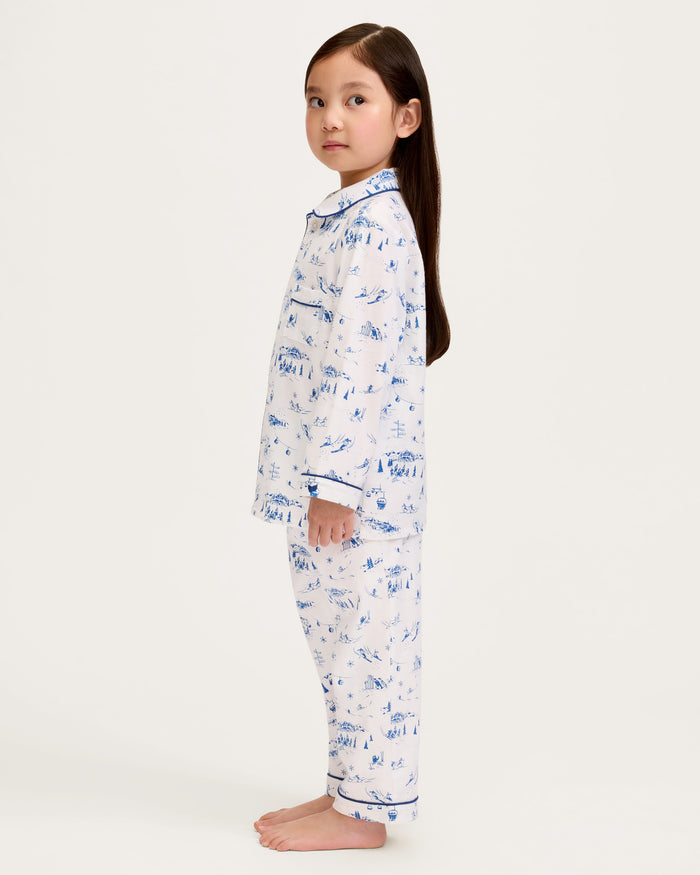 Kid's Twill Pajama Set in Chalet Toile, a white pajama set with blue piping and scenic print, includes a long-sleeve button-up top and matching pants, shown laid flat on a white background.
