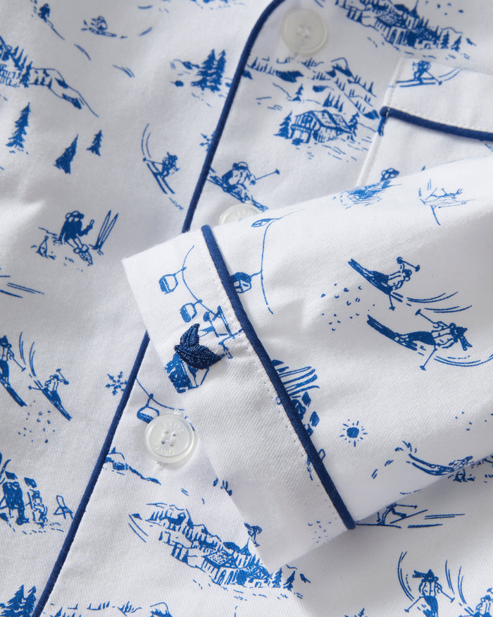 Kid's Twill Pajama Set in Chalet Toile, a white pajama set with blue piping and scenic print, includes a long-sleeve button-up top and matching pants, shown laid flat on a white background.