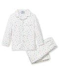 A child with short curly hair stands facing forward, wearing the Kid's Twill Pajama Set in Good Luck Charms—a white button-up pajama with a colorful pattern and matching pants—against a plain light background.