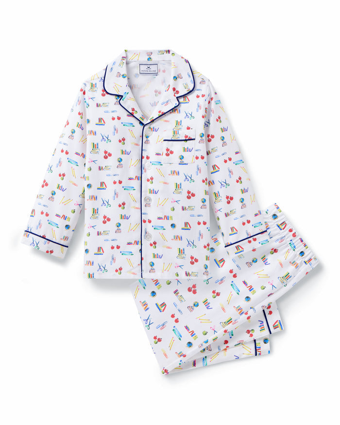 The Kid's Twill Pajama Set in Literary Lessons features a white collared, long-sleeve button-up top and matching pants with a colorful school-themed pattern and navy blue piping accents.