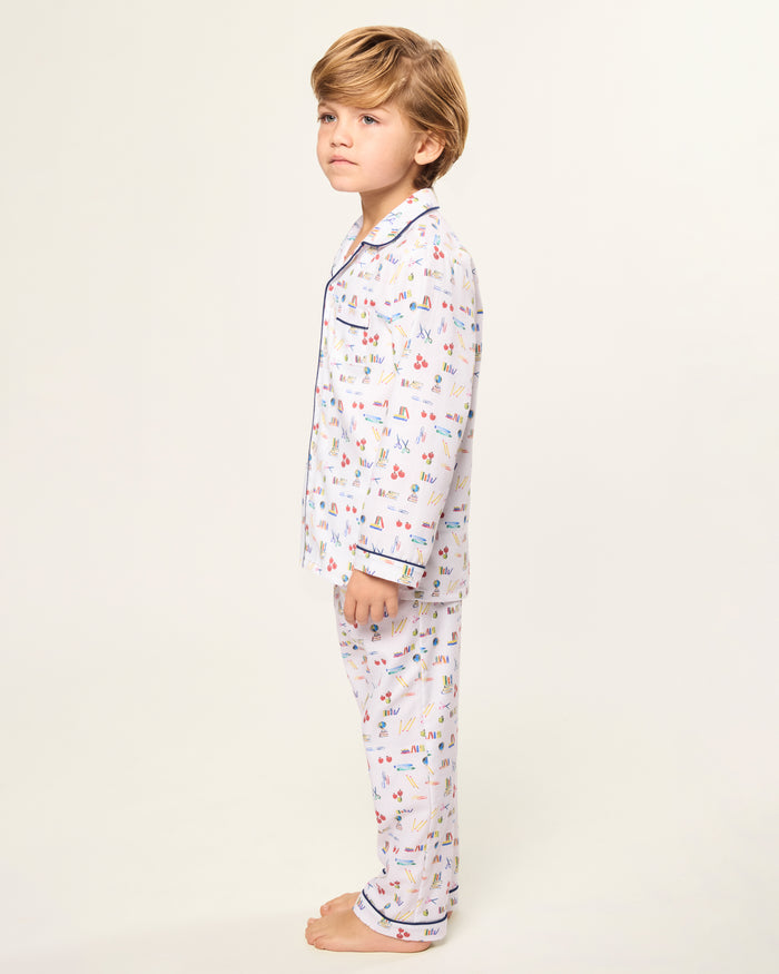 The Kid's Twill Pajama Set in Literary Lessons features a white collared, long-sleeve button-up top and matching pants with a colorful school-themed pattern and navy blue piping accents.