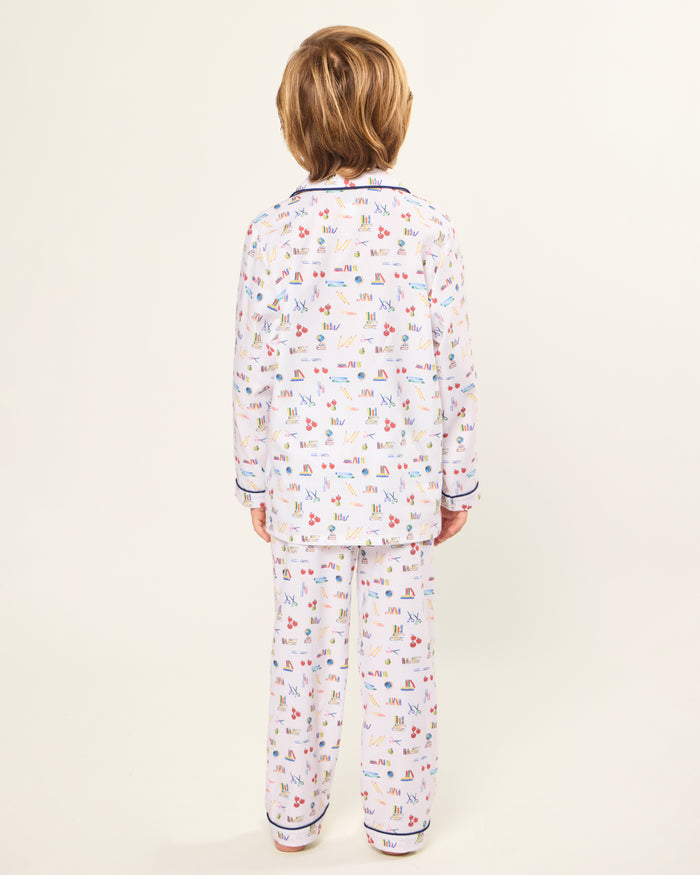 The Kid's Twill Pajama Set in Literary Lessons features a white collared, long-sleeve button-up top and matching pants with a colorful school-themed pattern and navy blue piping accents.