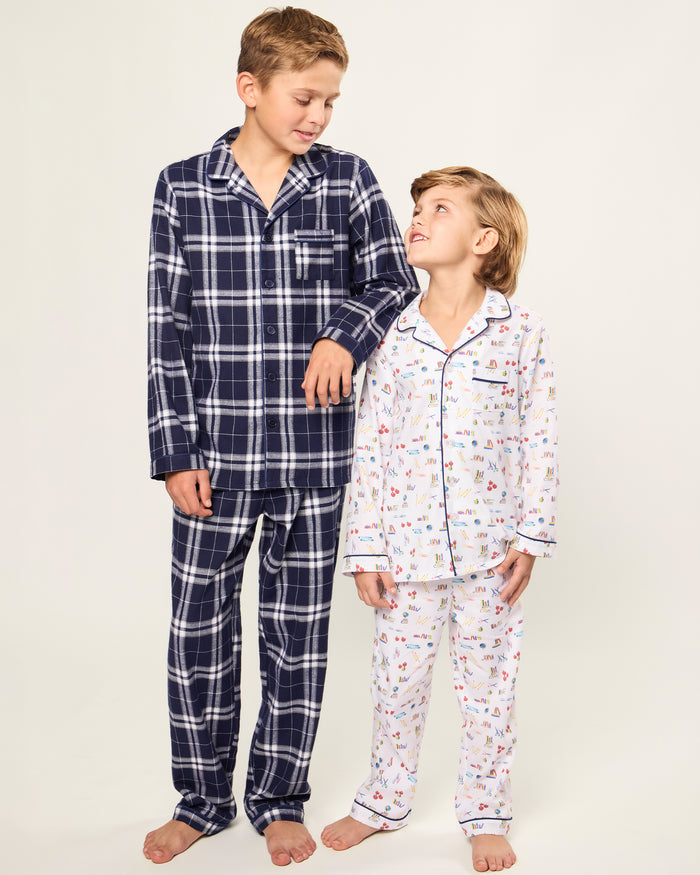 The Kid's Twill Pajama Set in Literary Lessons features a white collared, long-sleeve button-up top and matching pants with a colorful school-themed pattern and navy blue piping accents.