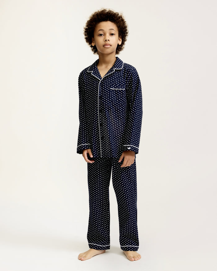 Kid's Twill Pajama Set in Midnight Hearts features navy blue pajamas with white heart prints, white piping, a long-sleeve button-up top with chest pocket, and matching pants.