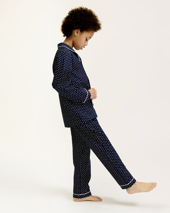 Kid's Twill Pajama Set in Midnight Hearts features navy blue pajamas with white heart prints, white piping, a long-sleeve button-up top with chest pocket, and matching pants.