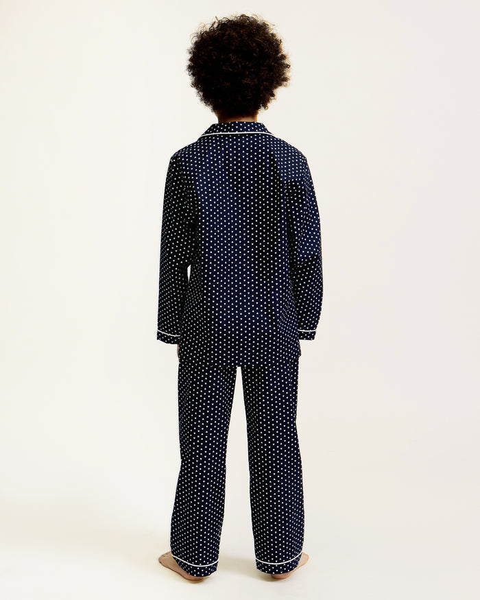 Kid's Twill Pajama Set in Midnight Hearts features navy blue pajamas with white heart prints, white piping, a long-sleeve button-up top with chest pocket, and matching pants.