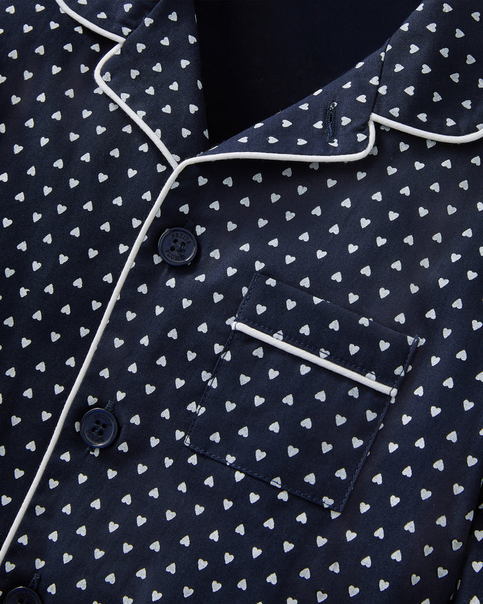 Kid's Twill Pajama Set in Midnight Hearts features navy blue pajamas with white heart prints, white piping, a long-sleeve button-up top with chest pocket, and matching pants.