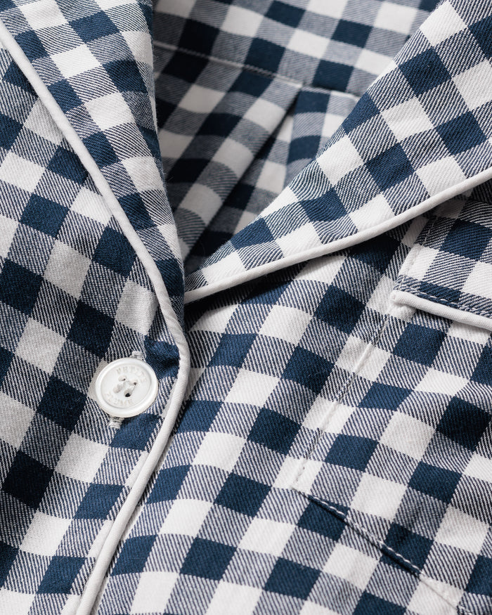 A close-up of the Kids Twill Pajama Set in Navy Gingham by Petite Plume showcases a blue and white gingham print fabric with a white button, highlighting the texture and detail perfect for stylish sleepwear.