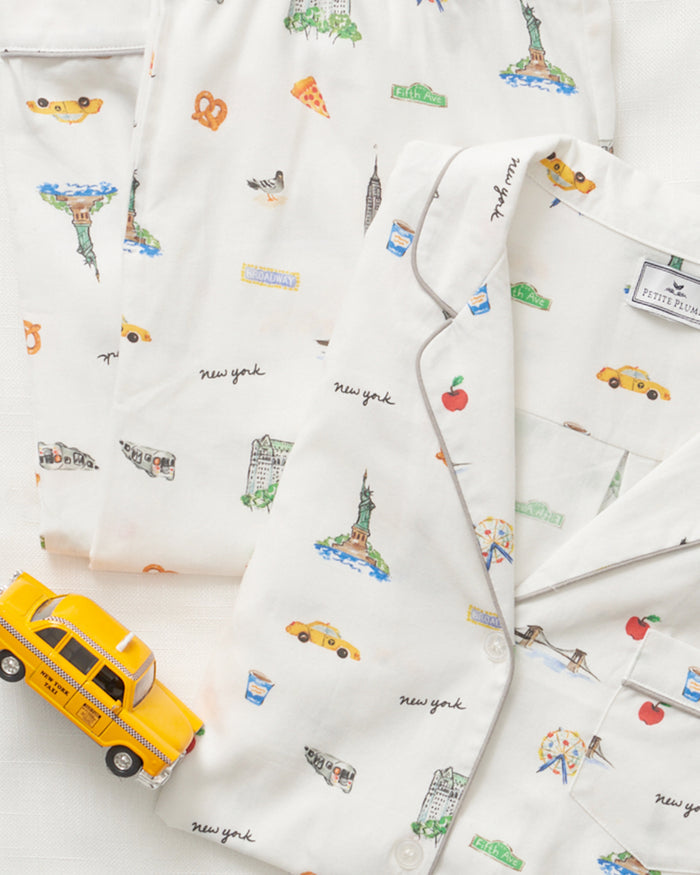The Kids Twill Pajama Set in New York! New York! by Petite Plume features a classic design with NYC illustrations like taxis, the Statue of Liberty, pizza, and pretzels. It also includes images of the Brooklyn Bridge and comes with a small yellow toy taxi.