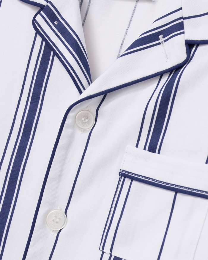 Close-up of the Kid’s Twill Pajama Set in Parlor Stripe, featuring a white pajama top with navy blue vertical stripes, coordinating white buttons, and a pocket trimmed with matching navy piping.