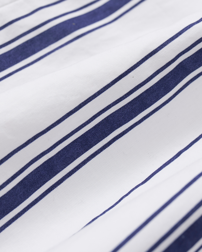 Featuring the Kid’s Twill Pajama Set in Parlor Stripe, this fabric showcases a crisp white base adorned with parallel navy blue stripes of varying thickness for a timeless, classic striped look. The twill material displays a softly wrinkled texture, adding to its relaxed appeal.