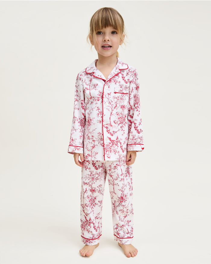The Kid's Twill Pajama Set in Red Timeless Toile features a white base with red toile print, long-sleeve button-up top with front pocket, matching pants, and red piping accents.