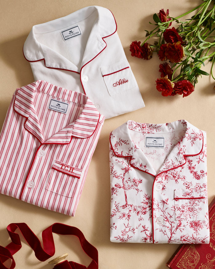 The Kid's Twill Pajama Set in Red Timeless Toile features a white base with red toile print, long-sleeve button-up top with front pocket, matching pants, and red piping accents.