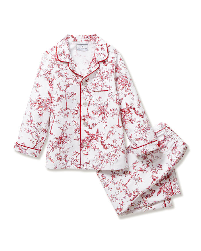 The Kid's Twill Pajama Set in Red Timeless Toile features a white base with red toile print, long-sleeve button-up top with front pocket, matching pants, and red piping accents.