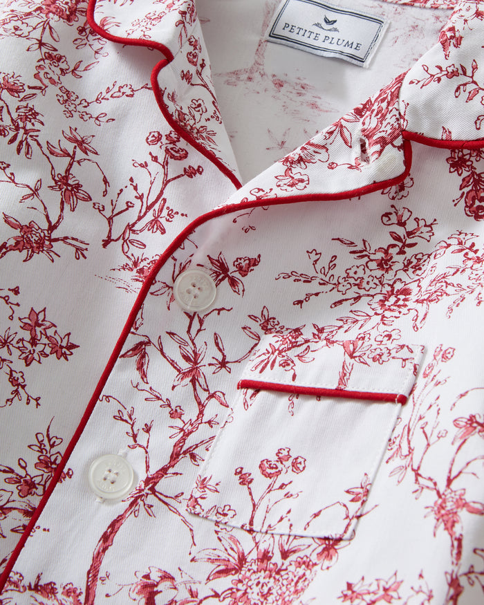 The Kid's Twill Pajama Set in Red Timeless Toile features a white base with red toile print, long-sleeve button-up top with front pocket, matching pants, and red piping accents.
