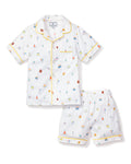 The Petite Plume Kids Twill Pajama Short Set in Birthday Wishes includes a short-sleeve, button-up shirt and shorts. The white fabric is decorated with colorful birthday fantasy prints of cakes, balloons, and party hats, featuring luxurious yellow piping on the cuffs and collar.