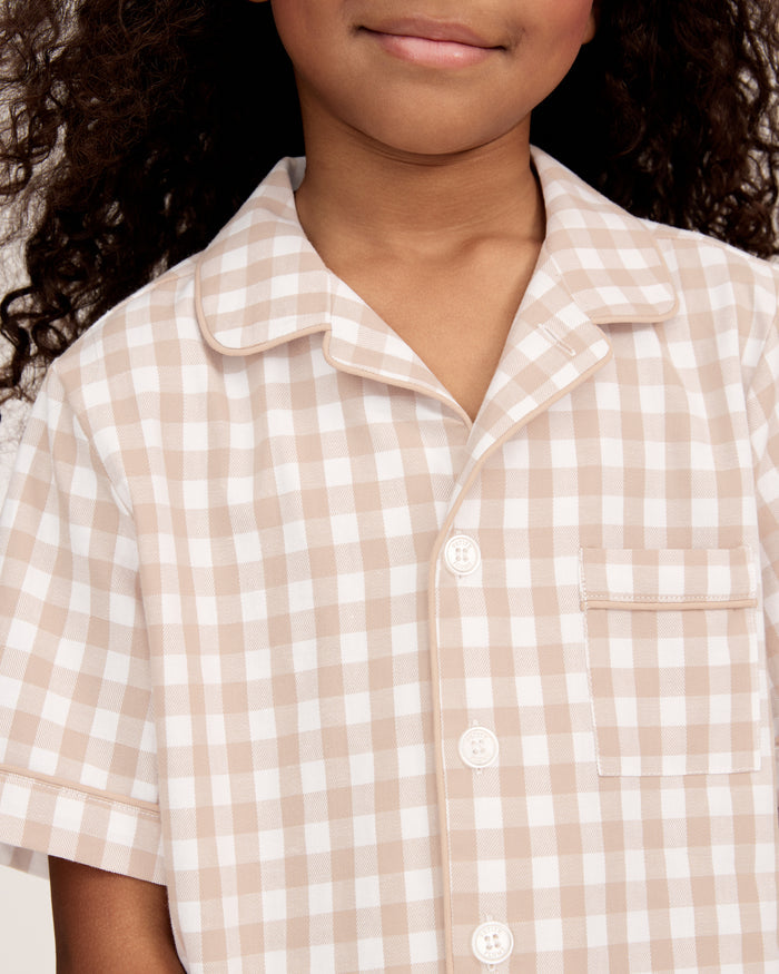 The Kid's Twill Pajama Short Set in Camel Gingham features a light beige and white gingham pattern with a collared, button-front top, chest pocket, and elastic waist shorts.