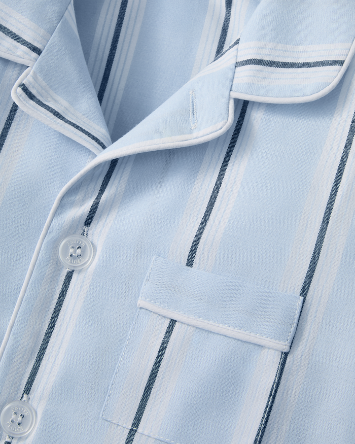 Close-up of the Kid’s Twill Pajama Short Set in Coastal Stripe, featuring a light blue button-up pajama shirt with white and dark blue vertical stripes, a chest pocket, and white piping along the collar and pocket flap.