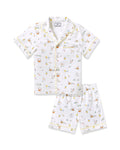 Two smiling children in luxurious Petite Plume sleepwear sit on the floor. They sport matching Kids Twill Short Sets in an Easter Frolic print. One child cuddles a stuffed bunny, embodying comfort and joy against a plain backdrop.