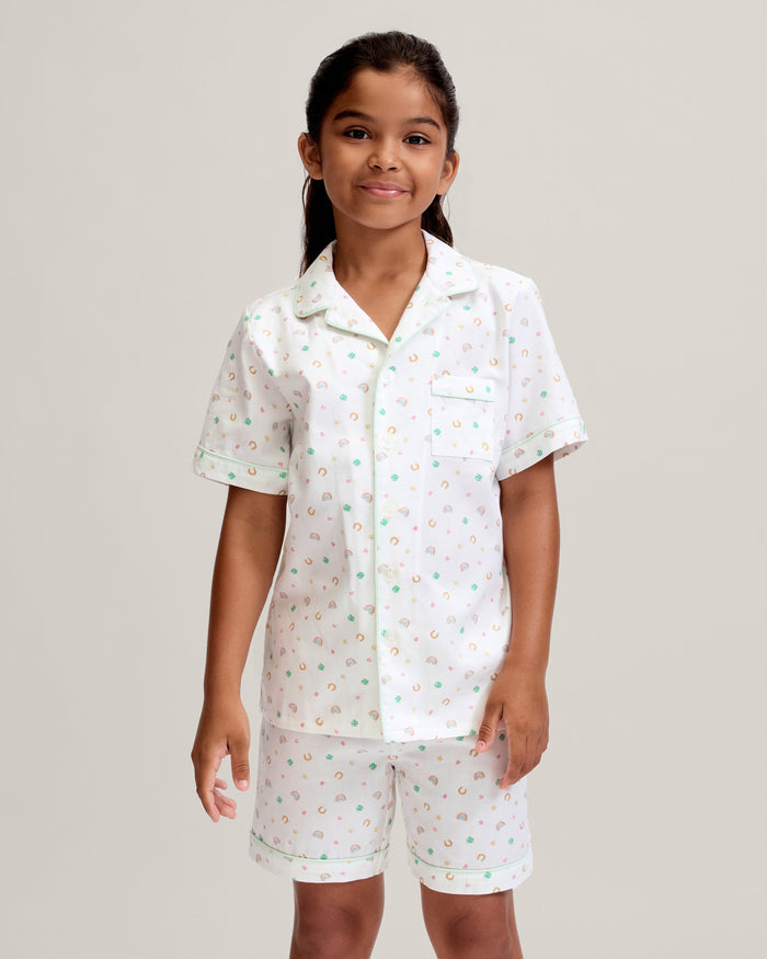 Young girl wearing a white outfit with colorful patterns on a plain background