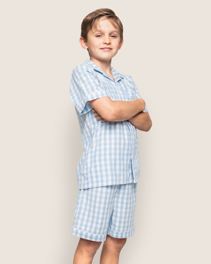 The Kid's Twill Pajama Short Set in Light Blue Gingham features a button-up short-sleeve top with a chest pocket and matching elastic-waist shorts in a classic gingham check pattern.