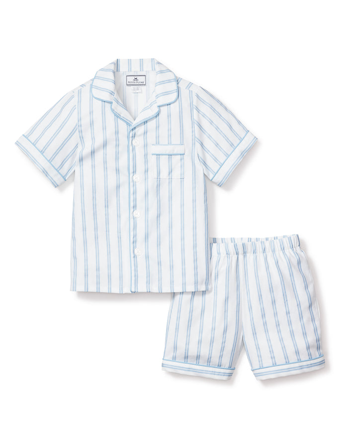 The Petite Plume Kids Twill Pajama Short Set in Periwinkle and White Stripe features soft, yarn-dyed cotton with a button-up shirt, chest pocket, and matching elastic-waist shorts in a light blue and white vertical stripe pattern.