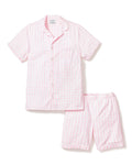 Three folded Petite Plume Kids Twill Pajama Short Sets in pink gingham rest on a textured surface, featuring charming designs of pink hearts, floral toile patterns, and pink stripes. Crafted from yarn-dyed cotton, they exude quality. Elegantly surrounded by white flowers for enhanced presentation.