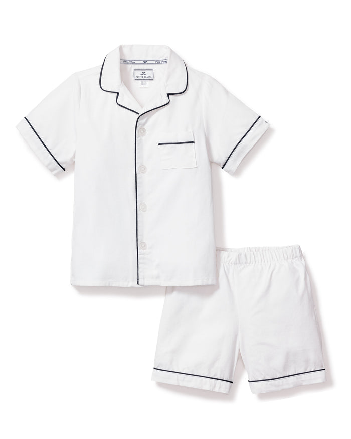 Experience luxurious sleepwear with Petite Plumes Kids Twill Pajama Short Set. Made from yarn-dyed cotton, it includes a white short-sleeve button-up shirt with navy piping and a chest pocket, paired with matching shorts featuring an elastic waistband for ultimate comfort.