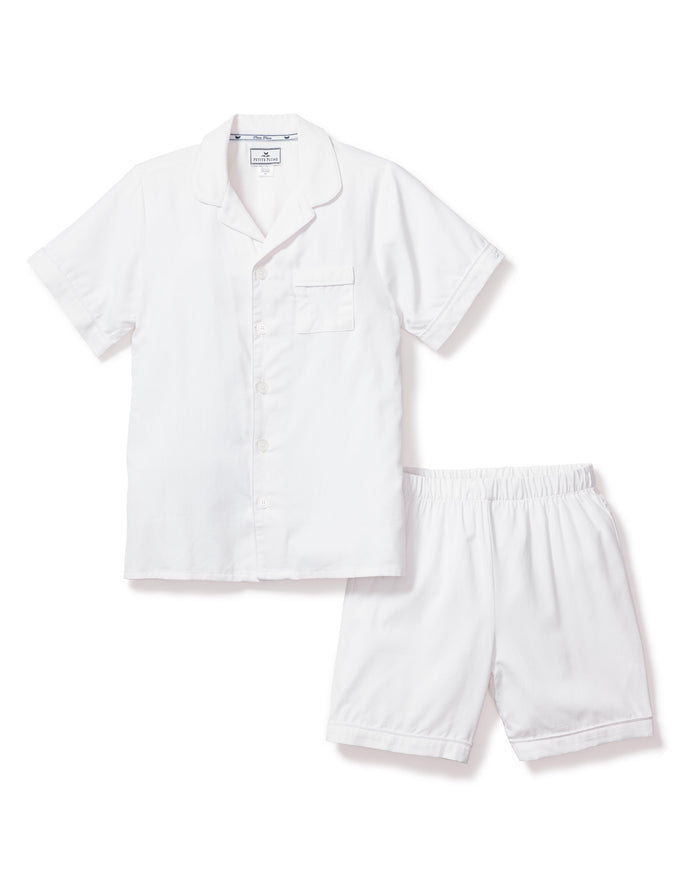 The Kids Twill Pajama Short Set in White by Petite Plume is a neat ensemble made from yarn-dyed cotton, featuring a short-sleeve button-up top with a chest pocket and matching elastic-waist shorts, set against a white background.