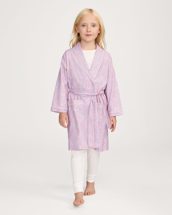 A young girl with blonde hair smiles as she ties the belt on her Kid's Twill Robe in Fleur Blush over a white nightgown.