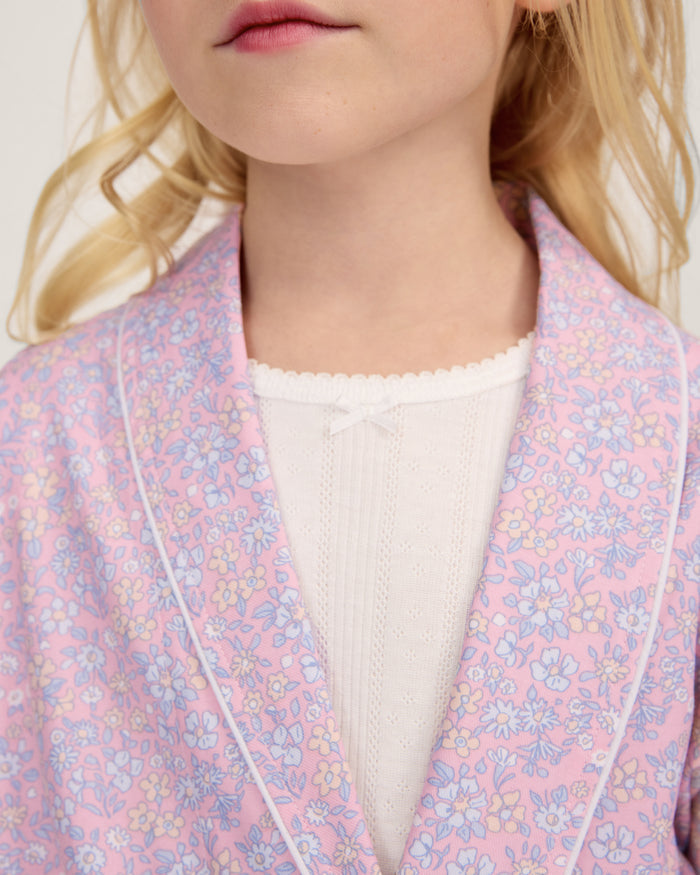 A young girl with blonde hair smiles as she ties the belt on her Kid's Twill Robe in Fleur Blush over a white nightgown.