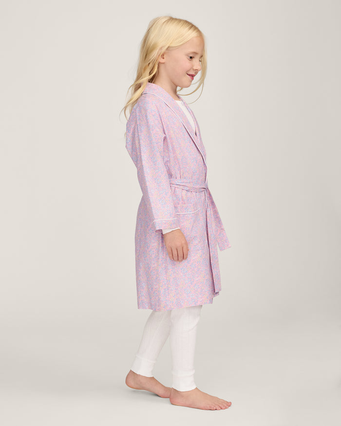 A young girl with blonde hair smiles as she ties the belt on her Kid's Twill Robe in Fleur Blush over a white nightgown.