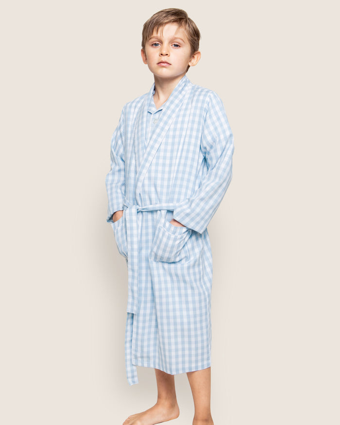 The Kid's Twill Robe in Light Blue Gingham features a soft gingham pattern, long sleeves, shawl collar, front pockets, and a matching belt at the waist for comfort and style.