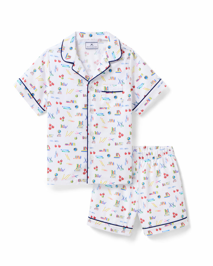 The Kid's Twill Short Set in Literary Lessons features a white base with colorful school-themed prints—pencils, books, and erasers—plus navy piping on the collar, pocket, sleeves, and shorts.