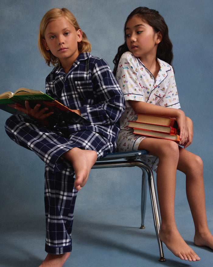 The Kid's Twill Short Set in Literary Lessons features a white base with colorful school-themed prints—pencils, books, and erasers—plus navy piping on the collar, pocket, sleeves, and shorts.