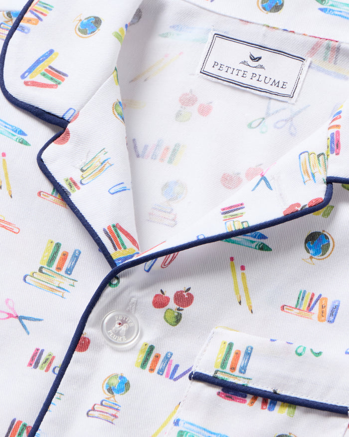 The Kid's Twill Short Set in Literary Lessons features a white base with colorful school-themed prints—pencils, books, and erasers—plus navy piping on the collar, pocket, sleeves, and shorts.