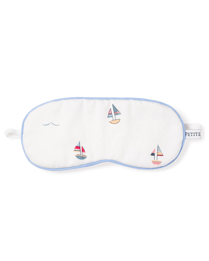 The Kids Twill Sleep Mask in Bateau by Petite Plume is a white luxury mask with blue trim, featuring small embroidered sailboats and waves. A PETITE tag on the right side makes it perfect for a matching set.