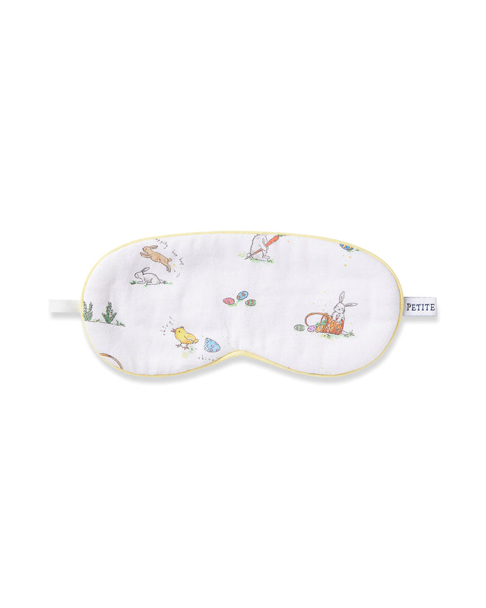 A young boy wears a Kid's Twill Sleep Mask in Easter Frolic, featuring colorful animal and nature prints, along with matching white pajamas. He smiles softly against a plain, light background.