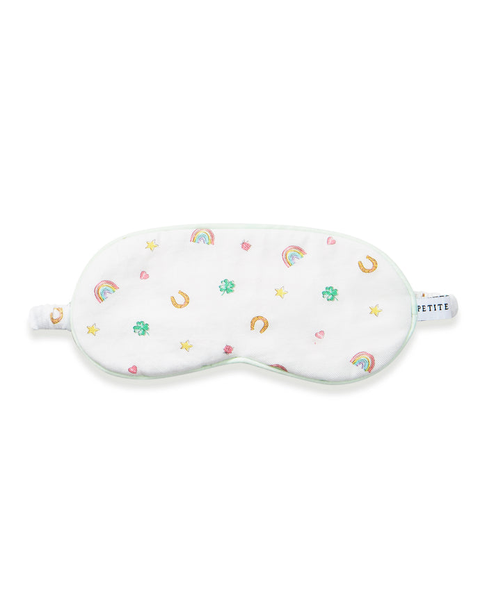 A young girl with long brown hair wears the Kid's Twill Sleep Mask in Good Luck Charms and a matching pajama top featuring rainbows, horseshoes, and clovers, standing against a neutral background.