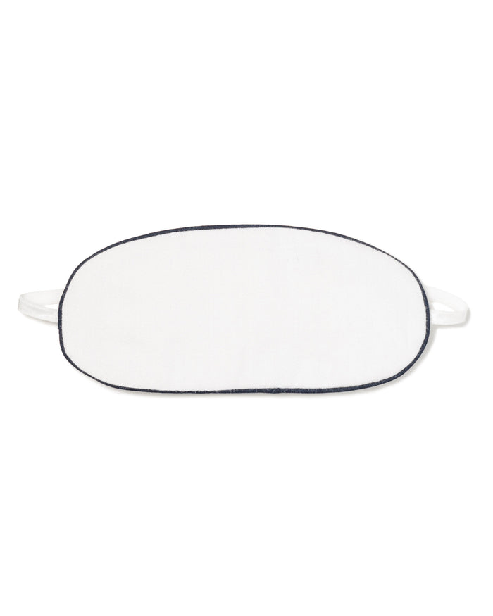 The Kids Twill Sleep Mask in White with Navy Piping by Petite Plume offers a touch of luxurious sleepwear. This oval-shaped mask is perfect for restful nights and pairs elegantly with other bedtime accessories, set gracefully against a white background.