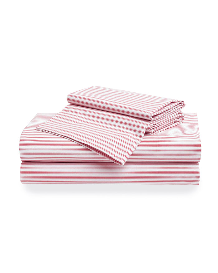 A neatly arranged stack of Petite Plume’s Luxe Premium 100% cotton bed sheets in an antique red ticking pattern features varied percale sheet sizes displaying stripes in diverse orientations against a plain white background.