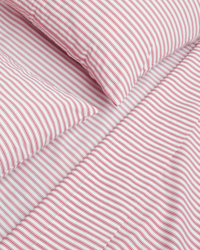 A neatly arranged stack of Petite Plume’s Luxe Premium 100% cotton bed sheets in an antique red ticking pattern features varied percale sheet sizes displaying stripes in diverse orientations against a plain white background.