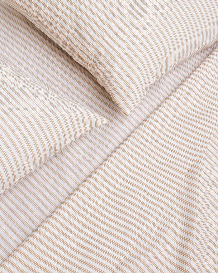 The Luxe Premium Percale Bed Sheets in Camel Ticking feature beige and white stripes and include a flat sheet, fitted sheet, and two pillowcases, all neatly folded and displayed on a white background.