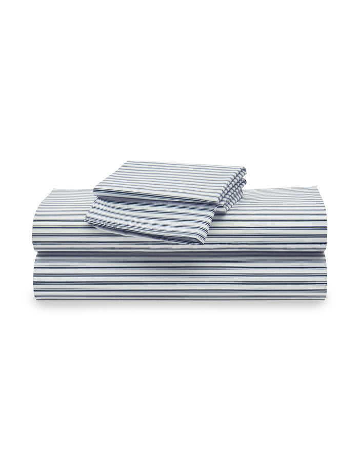 A stack of neatly folded Luxe Premium Cotton Bed Sheets in Navy French Ticking by Petite Plume is seen. Crafted from 100% cotton percale, the set includes a flat sheet, fitted sheet, and two pillowcases.