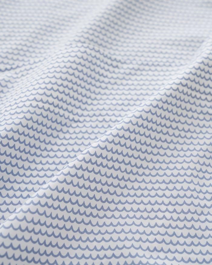 The Luxe Premium Cotton La Mer Bed Sheets by Petite Plume feature a pattern of small, evenly spaced blue scallops on a white background, creating a wave-like effect. The breathable cotton fabric offers a slightly creased texture for added depth and elegance.