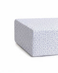 A close-up of a mattress corner covered with the Luxe Premium Percale Crib Sheet in Ditsy Waltz White, featuring a small blue floral pattern. The sheet fits snugly around the mattress.