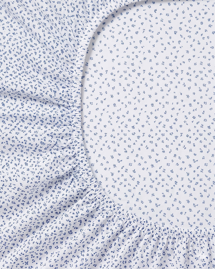 Close-up of the Luxe Premium Percale Crib Sheet in Ditsy Waltz White, showcasing its small blue floral patterns on a crisp white background and gathered elastic edges around an oval center section with the same delicate design.